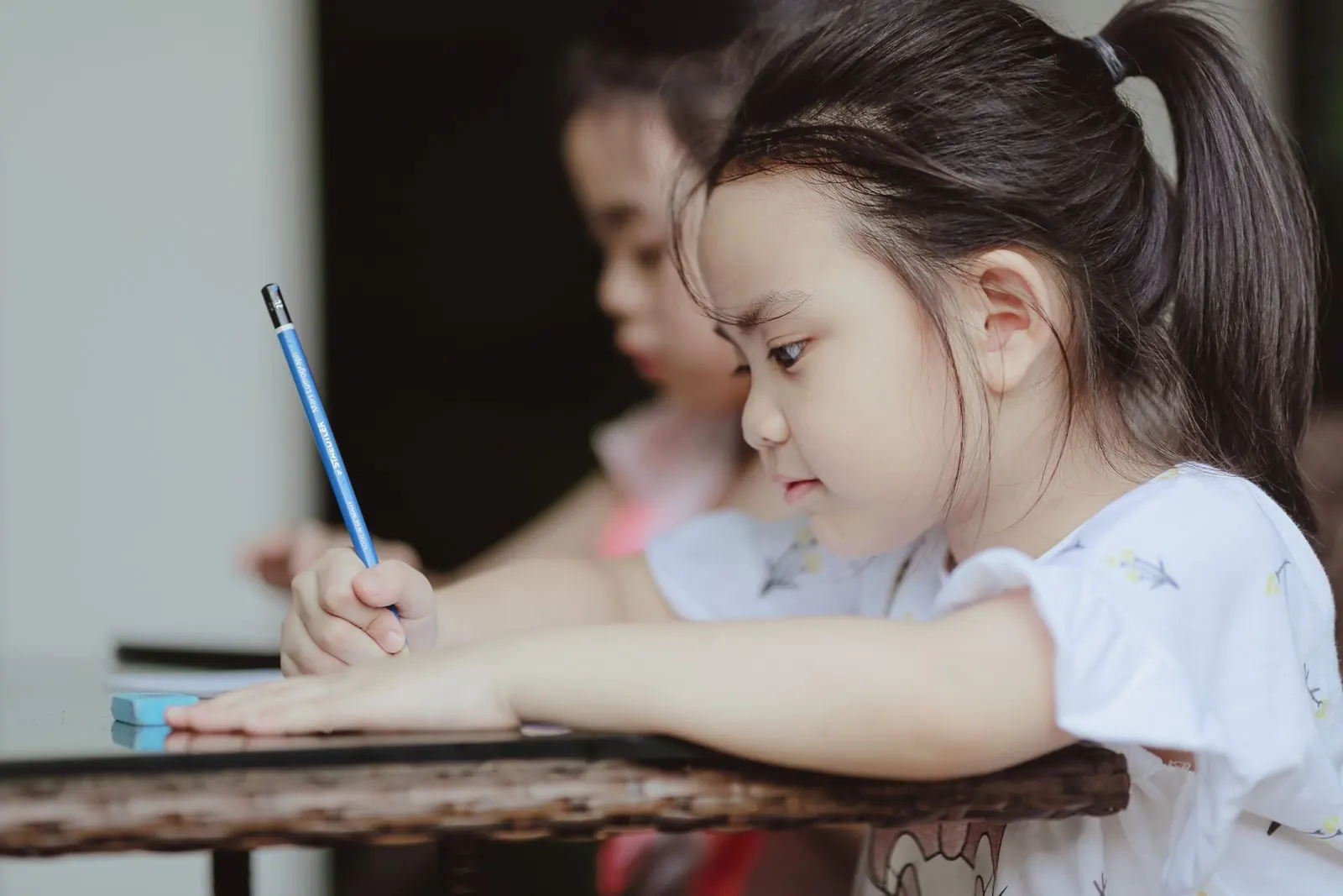 Bé gái cầm bút tập tô vẽ bên bàn học