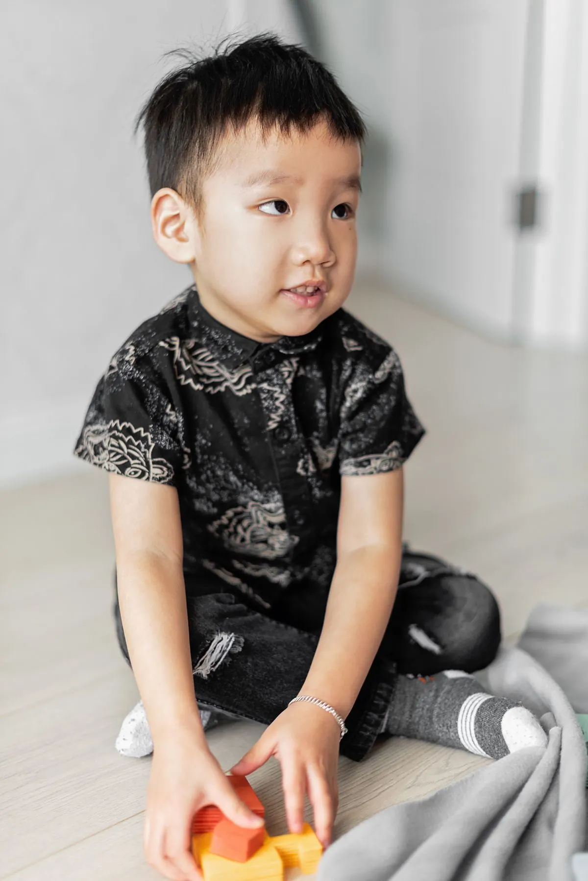 Bé trai ngồi chơi trên sàn nhà, tay cầm món đồ chơi nhỏ